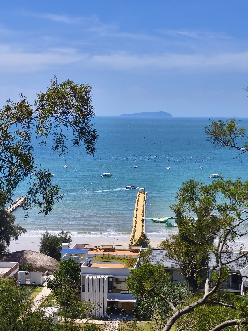 北海海湾远眺涠洲岛,海面上停着游船,岸边是通向海里的栈桥